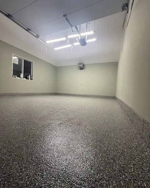 Garage with sage green walls, linear LED lights and a grey flake epoxy floor coved up the wall